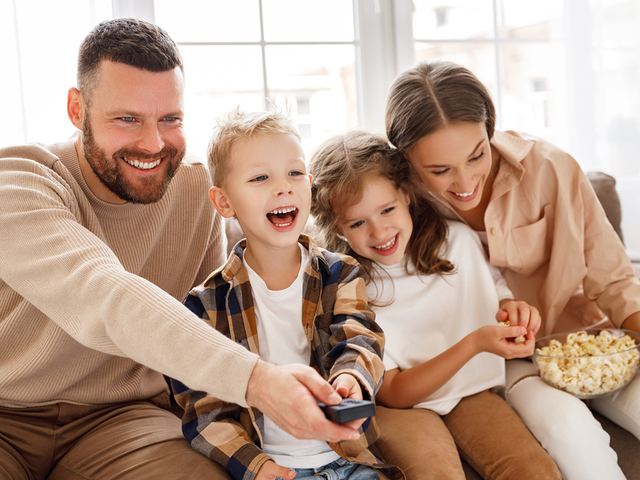 Eine Familie sitzt lachend zusammen und schaut Fernsehen.