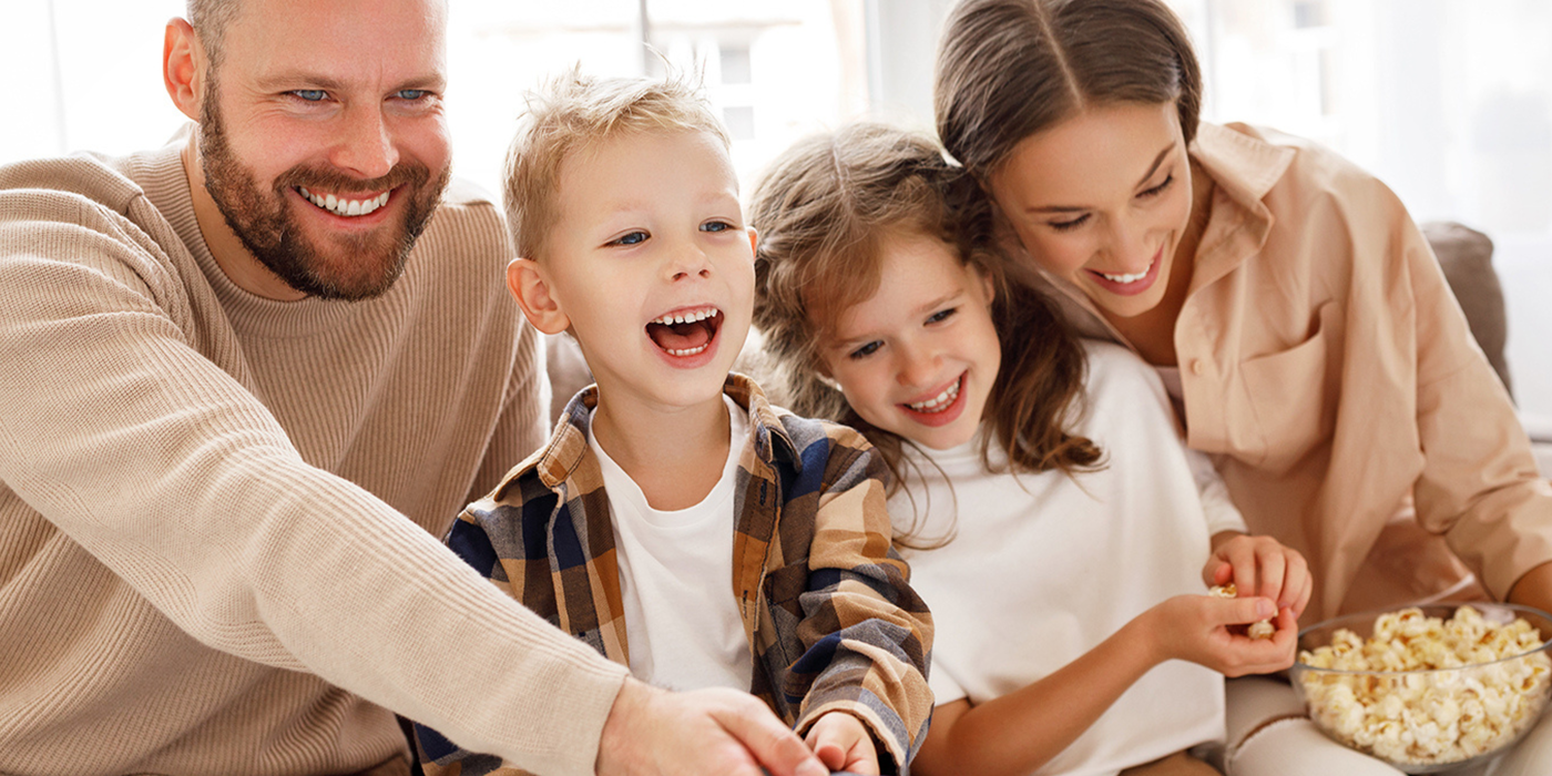 Eine Familie sitzt lachend zusammen und schaut Fernsehen.