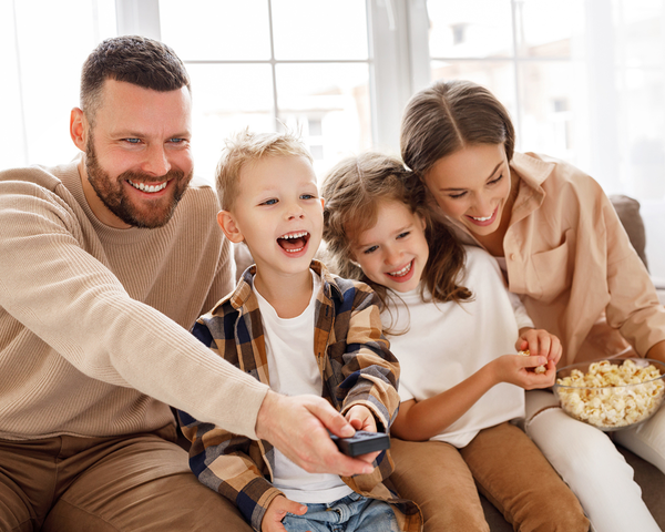 Eine Familie sitzt lachend zusammen und schaut Fernsehen.