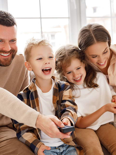 Eine Familie sitzt lachend zusammen und schaut Fernsehen.