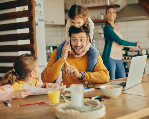 Mann mit Familie am Esszimmertisch vor dem Laptop