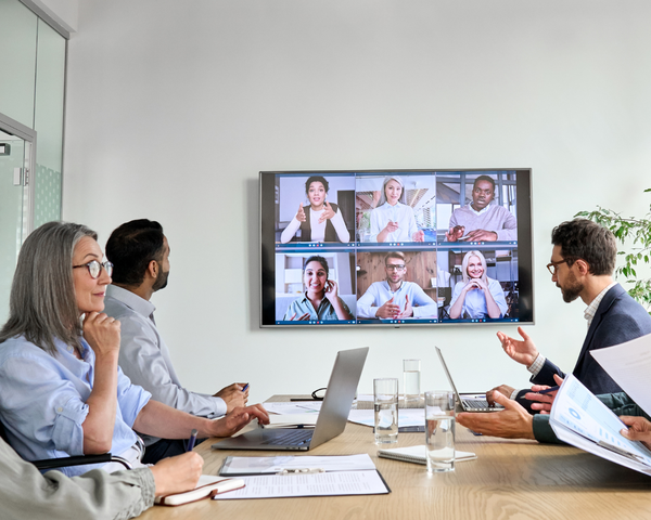 Digitale Zusammenarbeit im Unternehmen Videokonferenz in einem Konferenzraum mit mehreren Mitarbeitenden in einem größeren Unternehmen