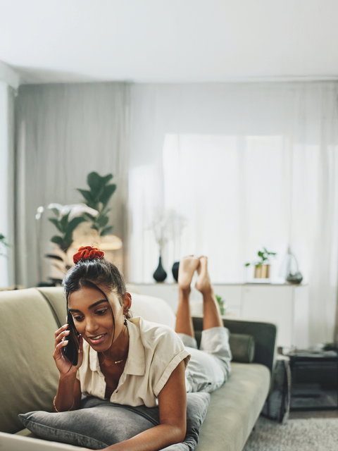 Frau telefoniert auf dem Sofa vor Laptop
