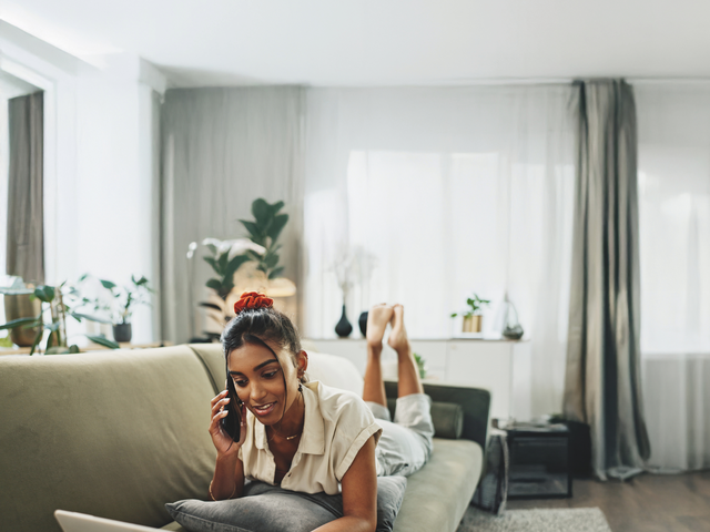 Frau telefoniert auf dem Sofa vor Laptop