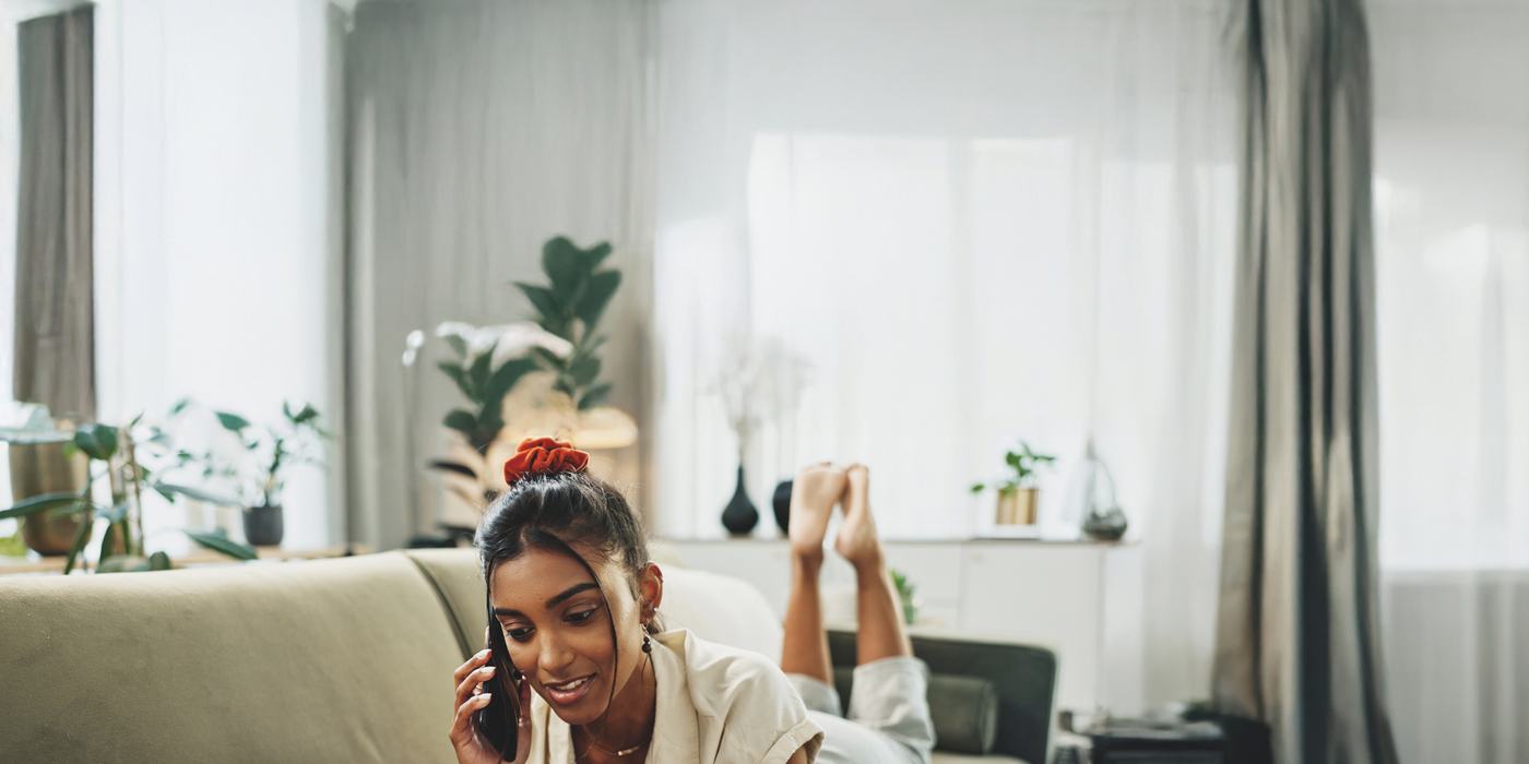 Frau telefoniert auf dem Sofa vor Laptop