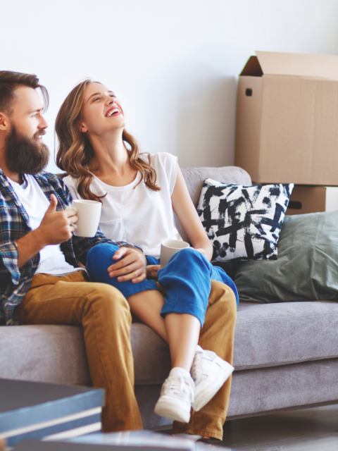 Frau und Mann sitzen auf dem Sofa, rundherum stehen Umzugskartons