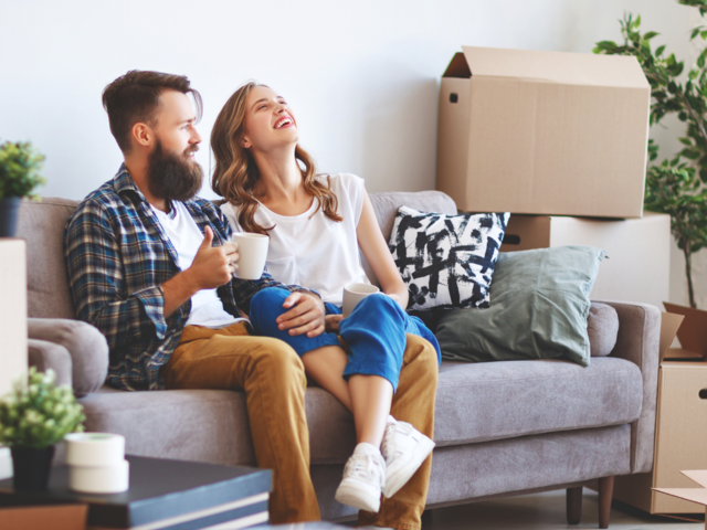 Frau und Mann sitzen auf dem Sofa, rundherum stehen Umzugskartons