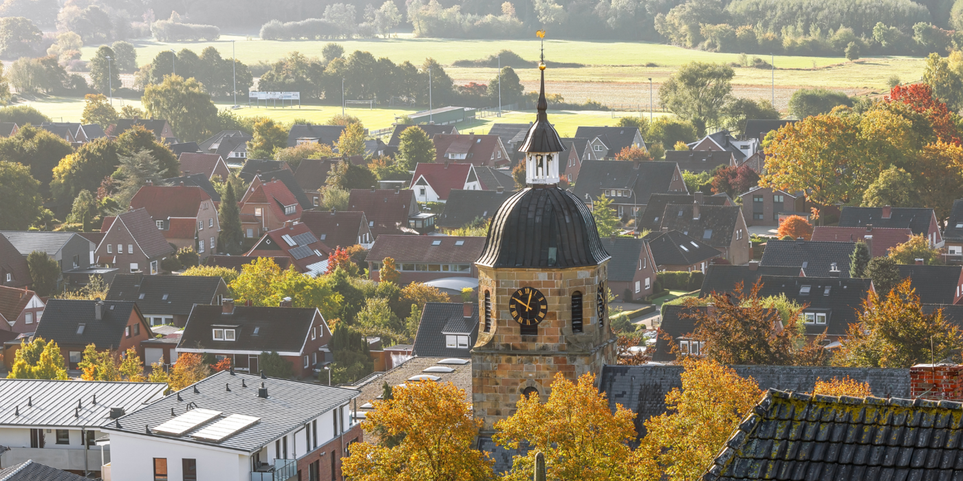 Ein Panorama aus der Grafschaft Bentheim mit Kirchturm, Einfamilienhäusern und bunt gefärbtem Laub – Sinnbild für regionale Verbundenheit und moderne Glasfaseranschlüsse direkt bis ins Haus.