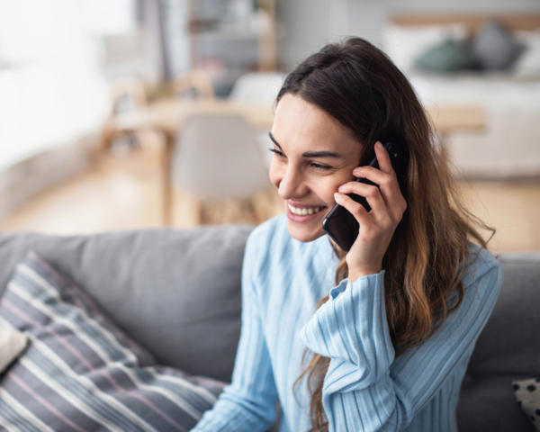 Frau sitzt auf dem Sofa und telefoniert mit dem Handy
