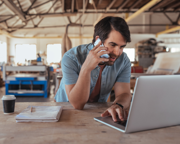 Mann telefoniert im Betrieb und arbeitet parallel am Laptop.