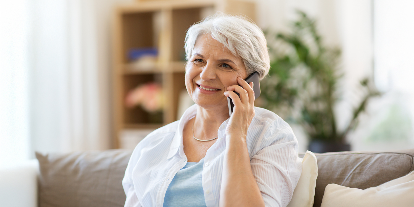 Eine lächelnde Seniorin sitzt entspannt auf dem Sofa und telefoniert – Symbol für vertraute Telefonnummern und gewohnte Erreichbarkeit, auch nach dem Anbieterwechsel.