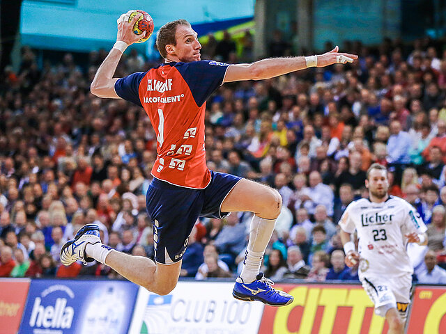 Ein Handballspieler springt während eines Spiels mit dem Ball in der Hand zum Wurf hoch