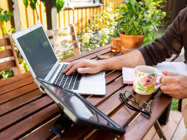 Person arbeitet draußen am Holztisch mit einem Laptop