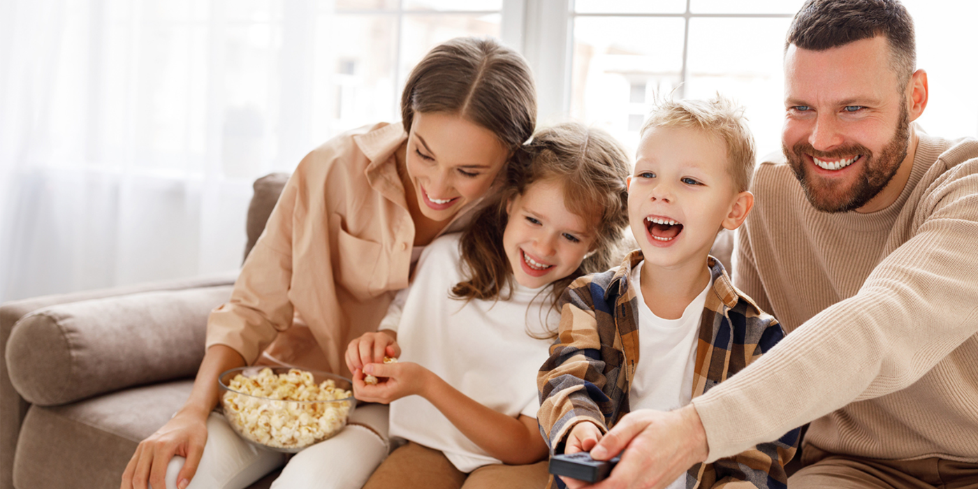 Eine Familie sitzt entspannt auf dem Sofa, schaut gemeinsam TV und hat Spaß – ideal als Symbolbild für modernes Fernsehen über Glasfaseranschluss.