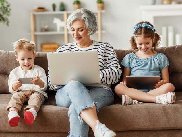 Oma sitzt mit ihren Enkeln vor dem Laptop auf der Couch