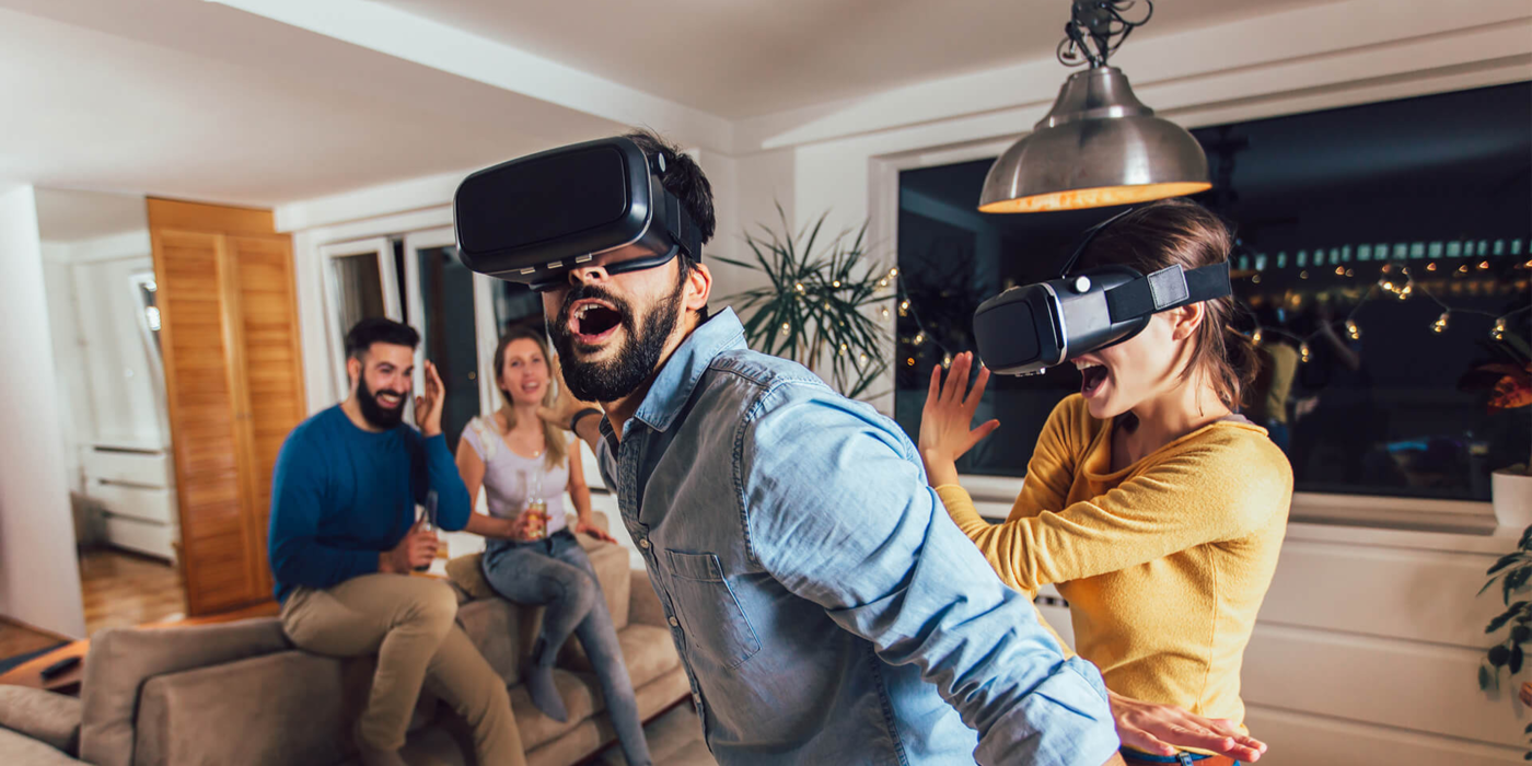 Zwei Personen tauchen mit VR-Brillen in virtuelle Welten ein, während Freunde auf dem Sofa begeistert zusehen – ein Symbol für moderne Unterhaltung mit schnellem Internet durch leistungsstarke Glasfaser-Tarife.