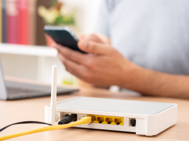 Nahaufnahme von einem Router, im Hintergrund sieht man Hände, die ein Handy bedienen