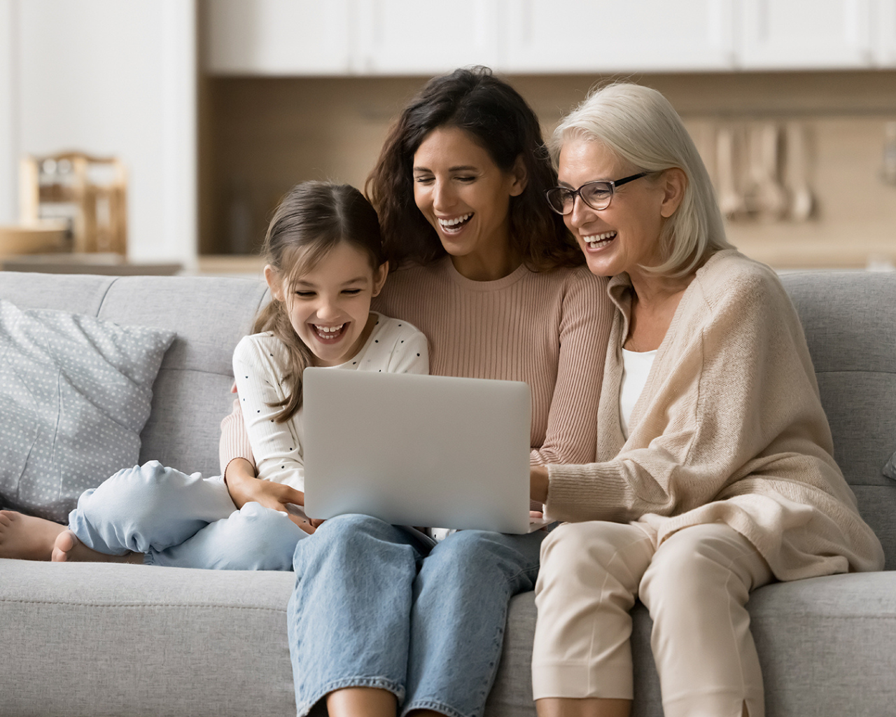 Zwei Frauen sitzen mit einem kleinen Mädchen auf dem Sofa und schauen zusammen auf den Bildschirm eine Notebboks