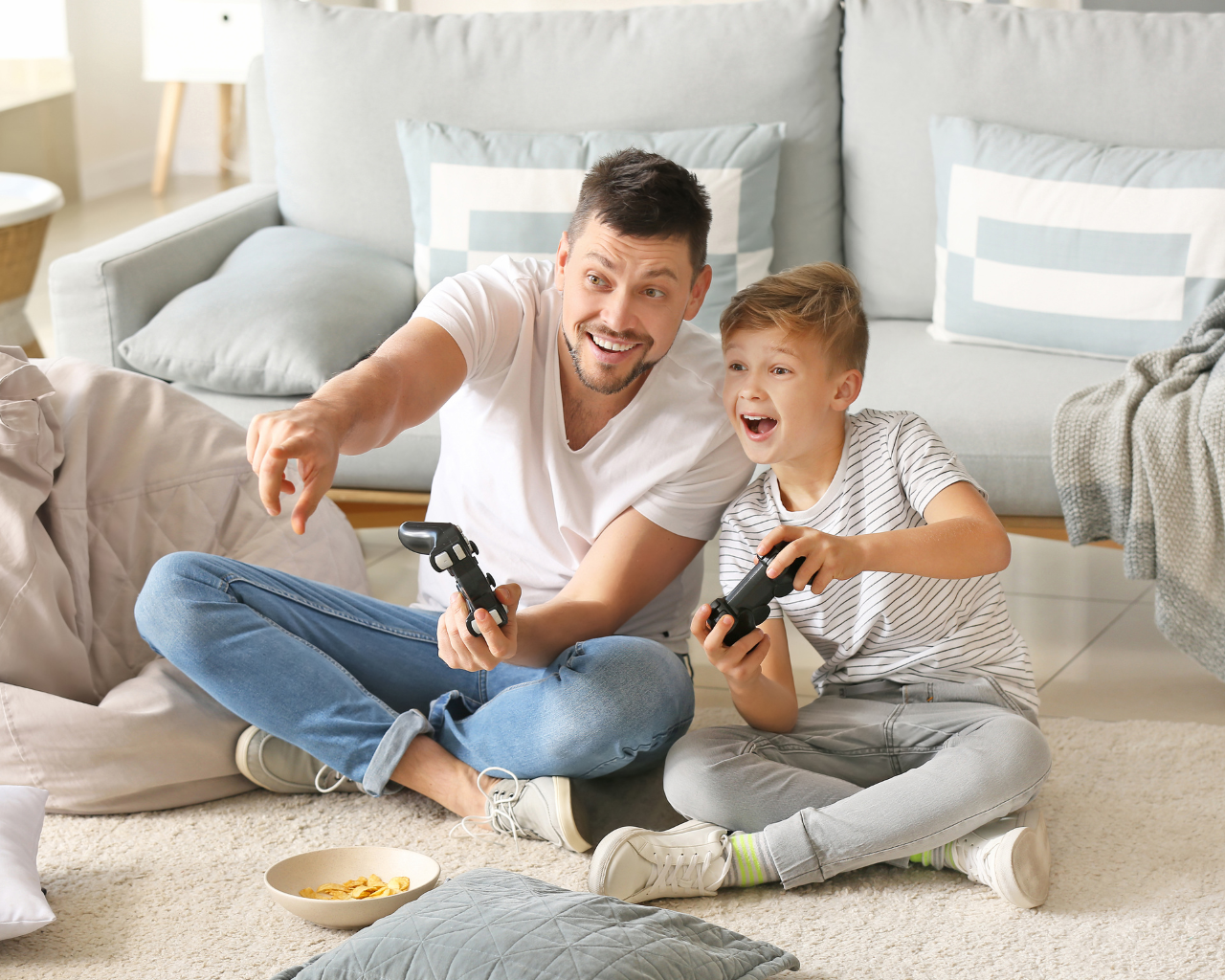 Vater und Sohn spielen gemeinsam begeistert mit Spielekonsole im Wohnzimmer.